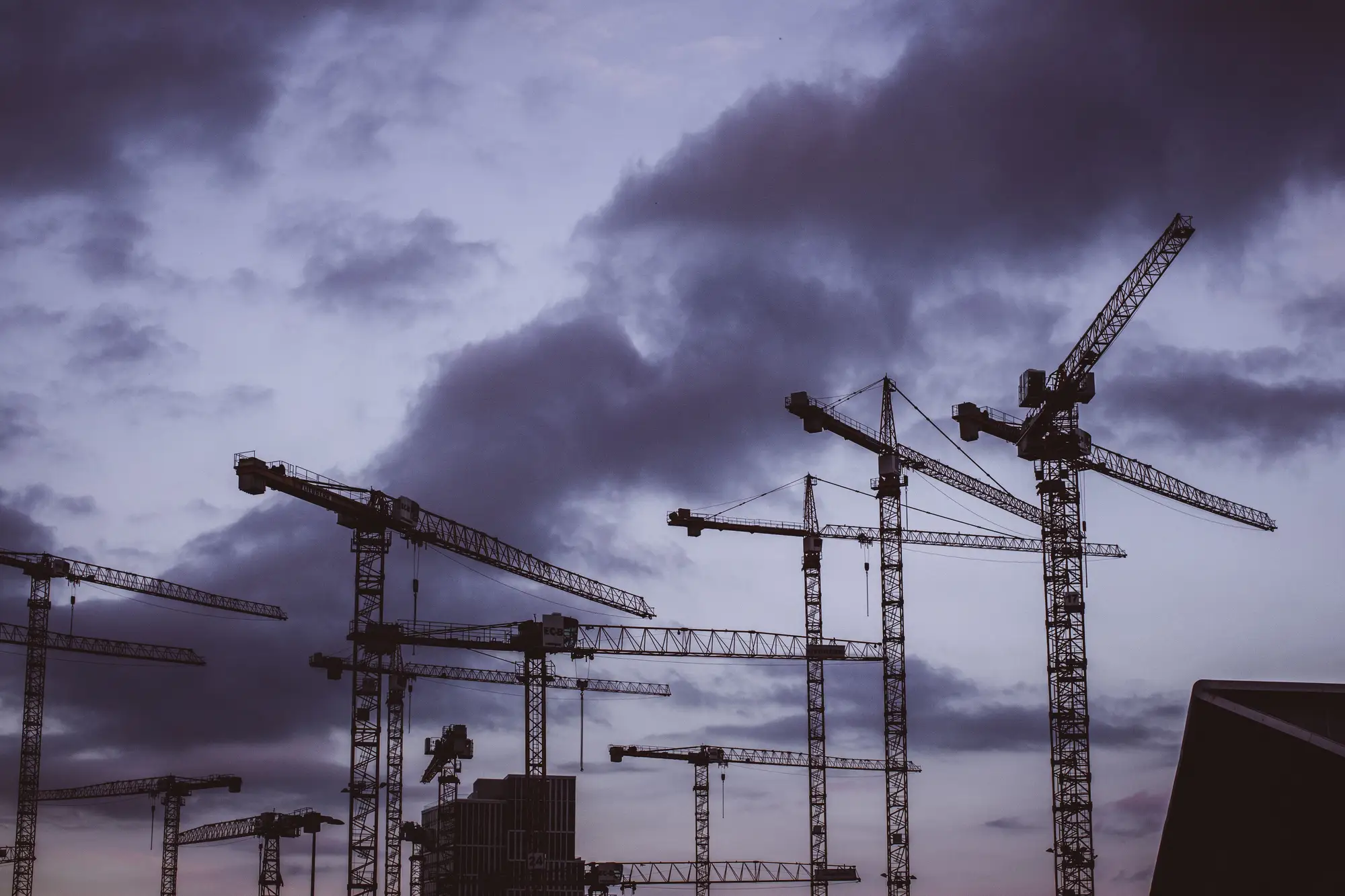 Tower cranes over a city building site against a dark evening sky