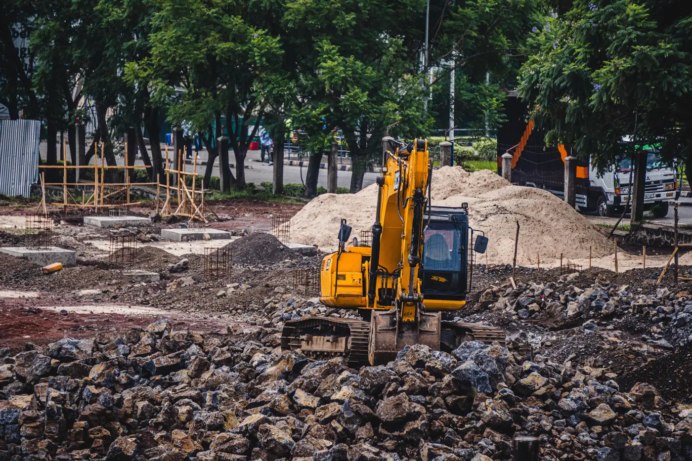 A yellow excavator working a pile of rubble and dirt at a construction site.