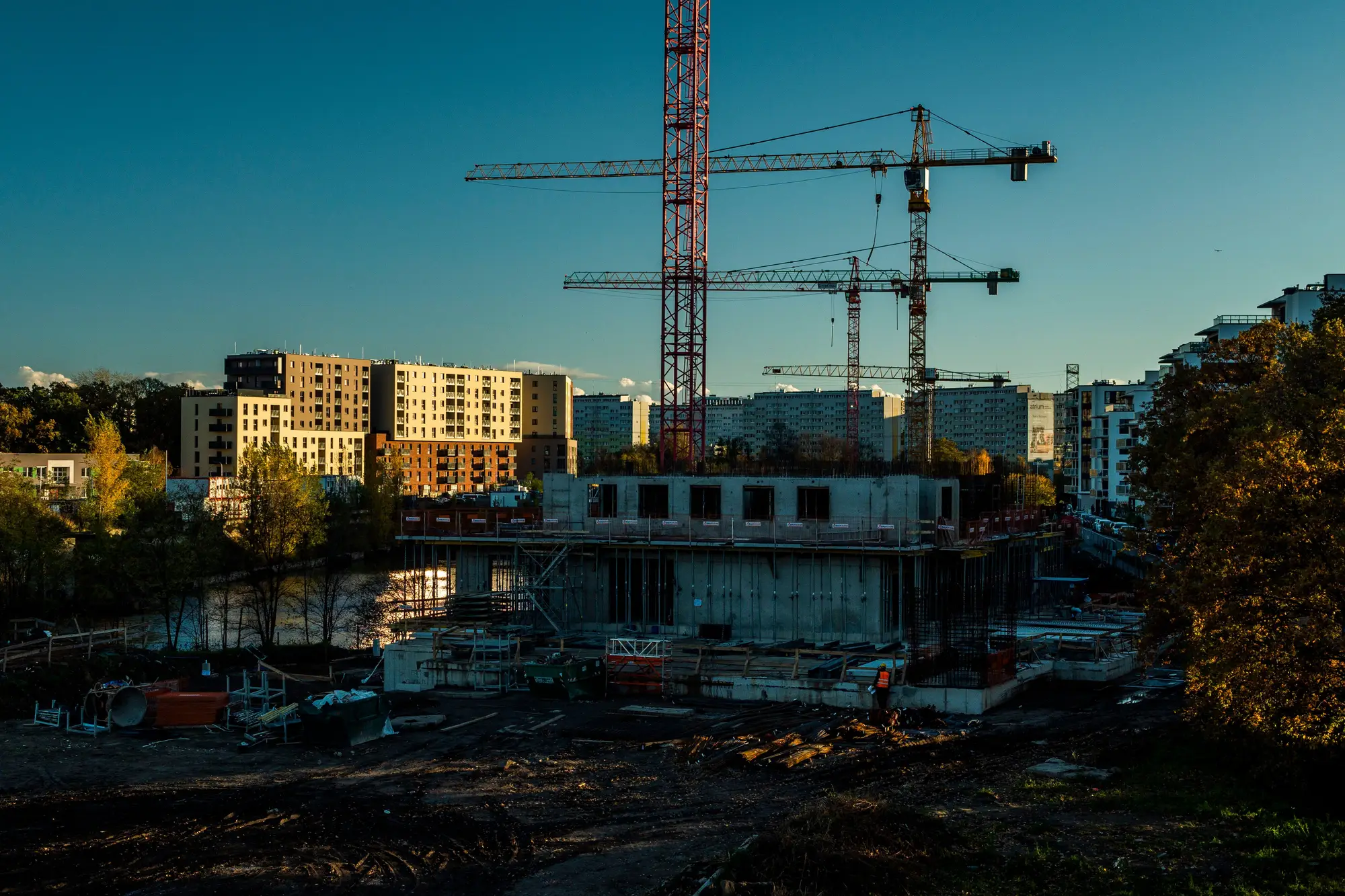 A concrete frame going up beside finished blocks, tower cranes overhead at dusk